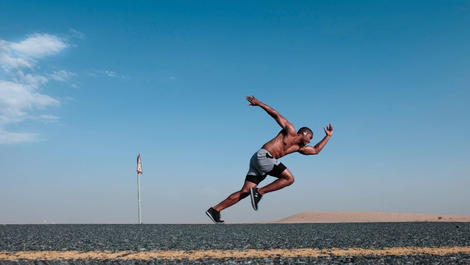 Sprinter exploding forward under a blue sky