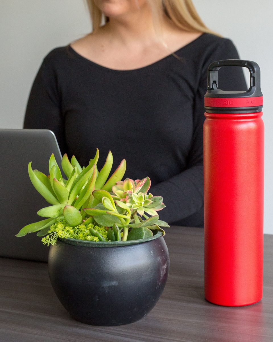 Red insulated water bottle on a desk next to a plant